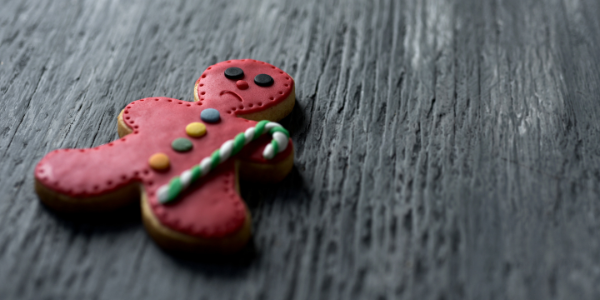 Image of a decorated gingerbread man cookie, laying on a table. He is holding a candy cane and frowning